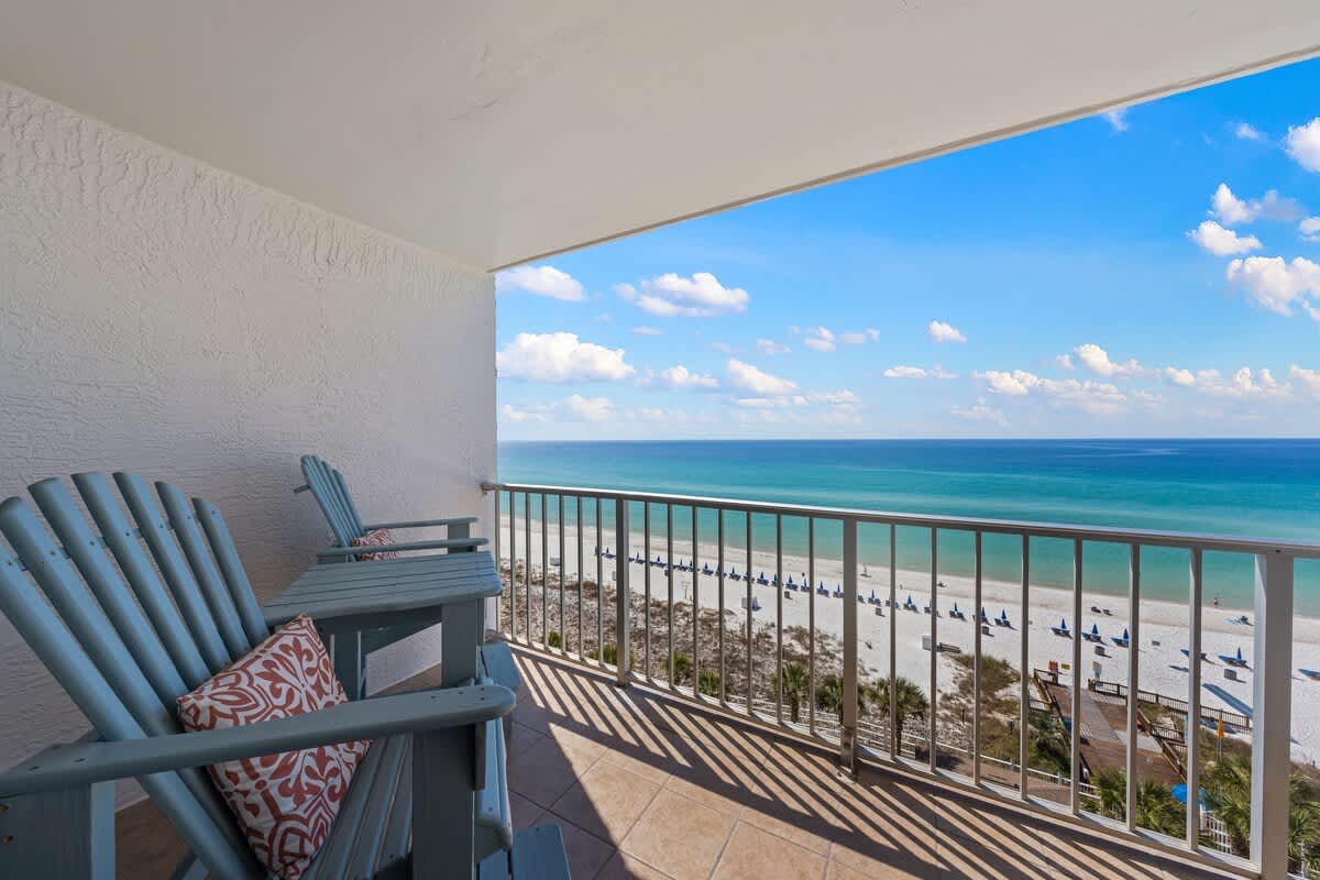 The Summit 919 – Balcony with blue chairs overlooking a sandy beach and ocean view.
