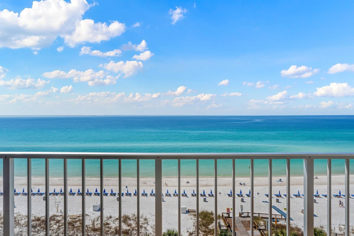 The Summit 919 – Ocean view from a balcony with beach chairs and umbrellas on a sandy shore.