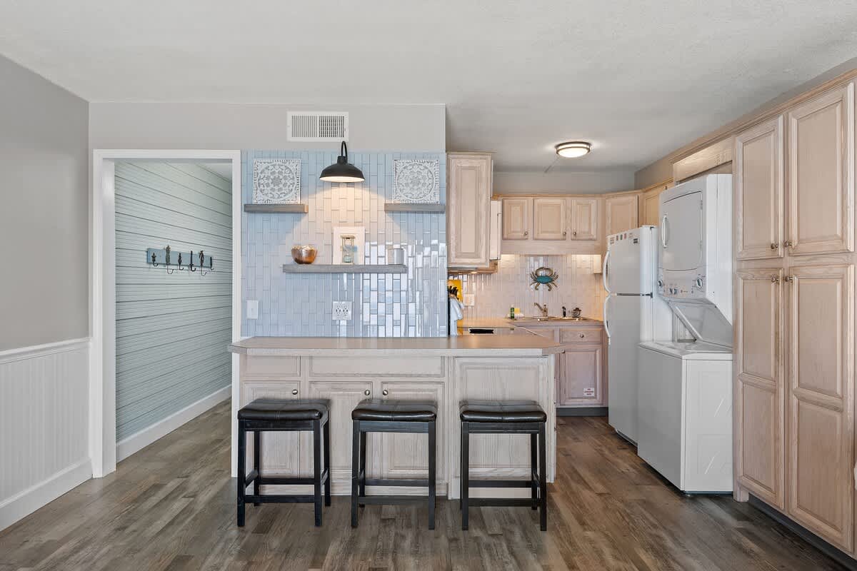 The Summit 919 – Kitchen with beige cabinets, blue tiled backsplash, bar seating, and washer/dryer units.