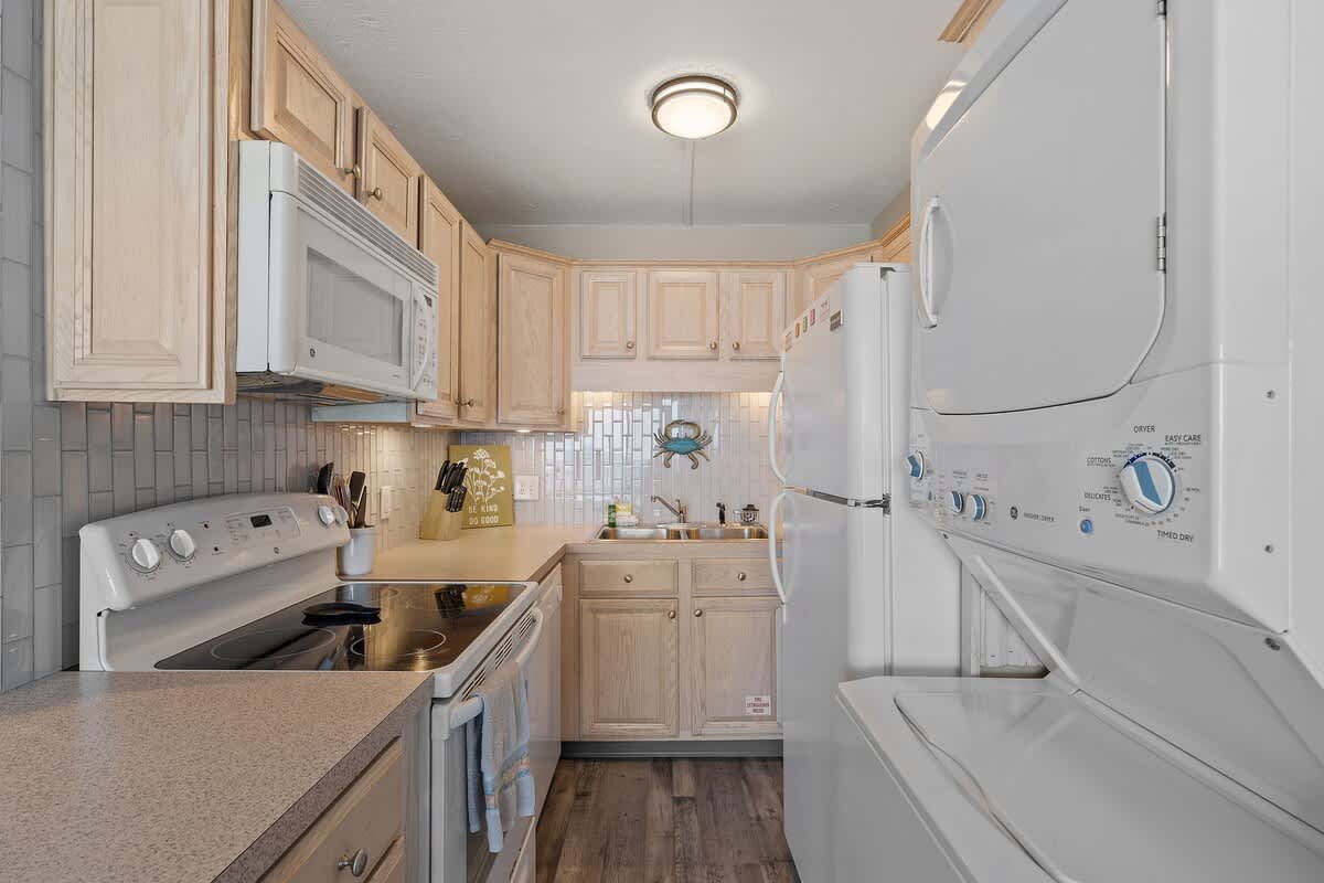 The Summit 919 – Compact kitchen with light wooden cabinets, stove, microwave, refrigerator, and stacked washer-dryer.