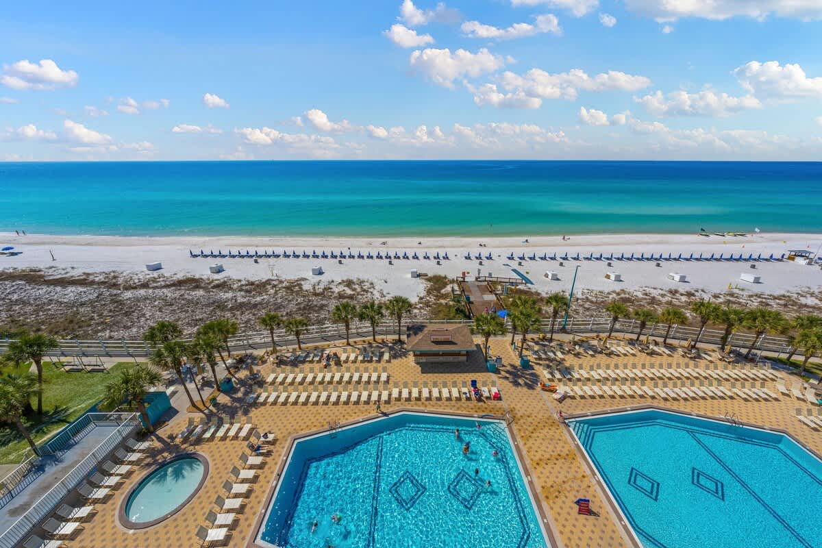 The Summit 919 – Aerial view of two pools, beach chairs, palm trees, and the ocean in the background.