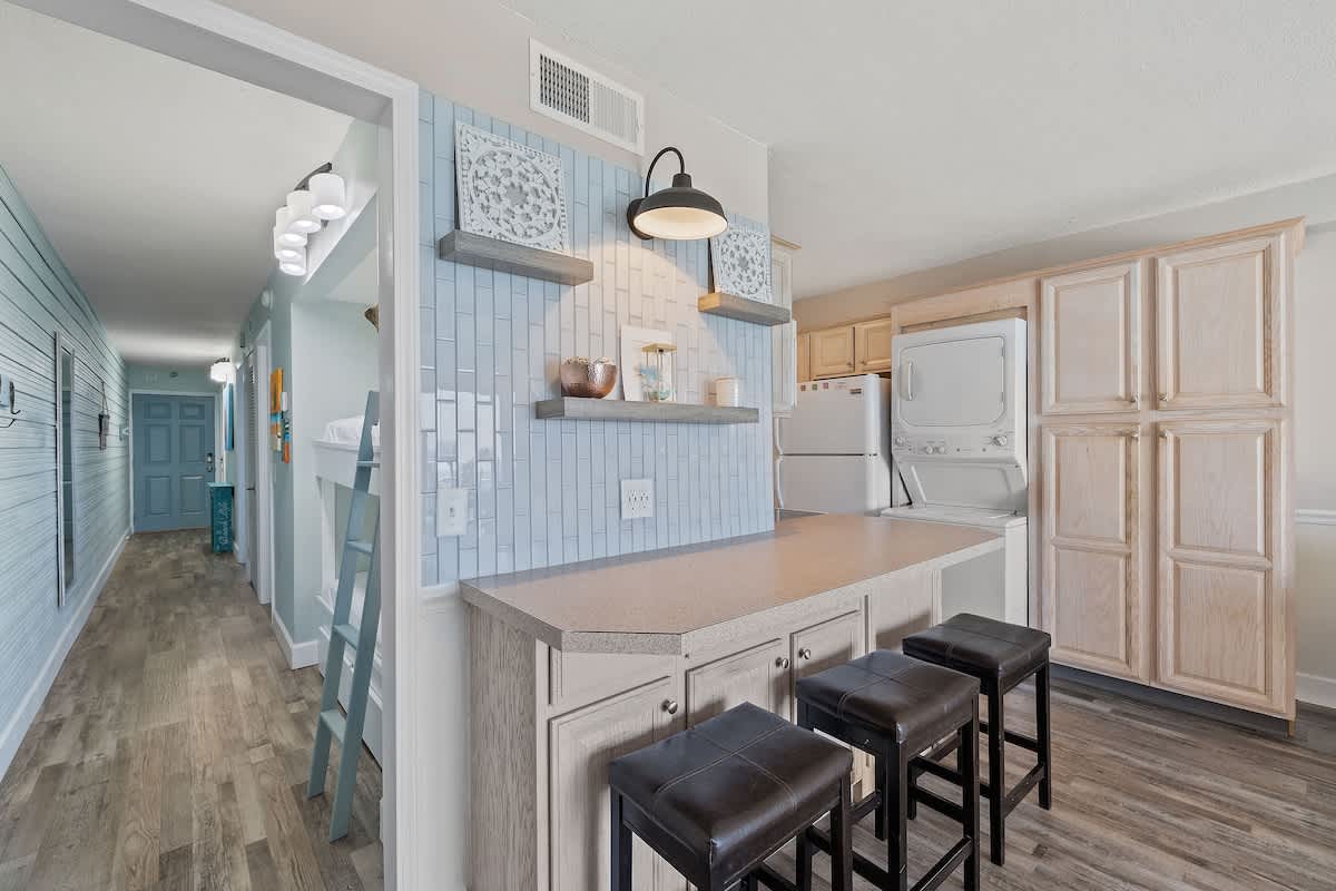 The Summit 919 – Open-concept kitchen with bar stools, light blue backsplash, and laundry appliances in a vacation rental.