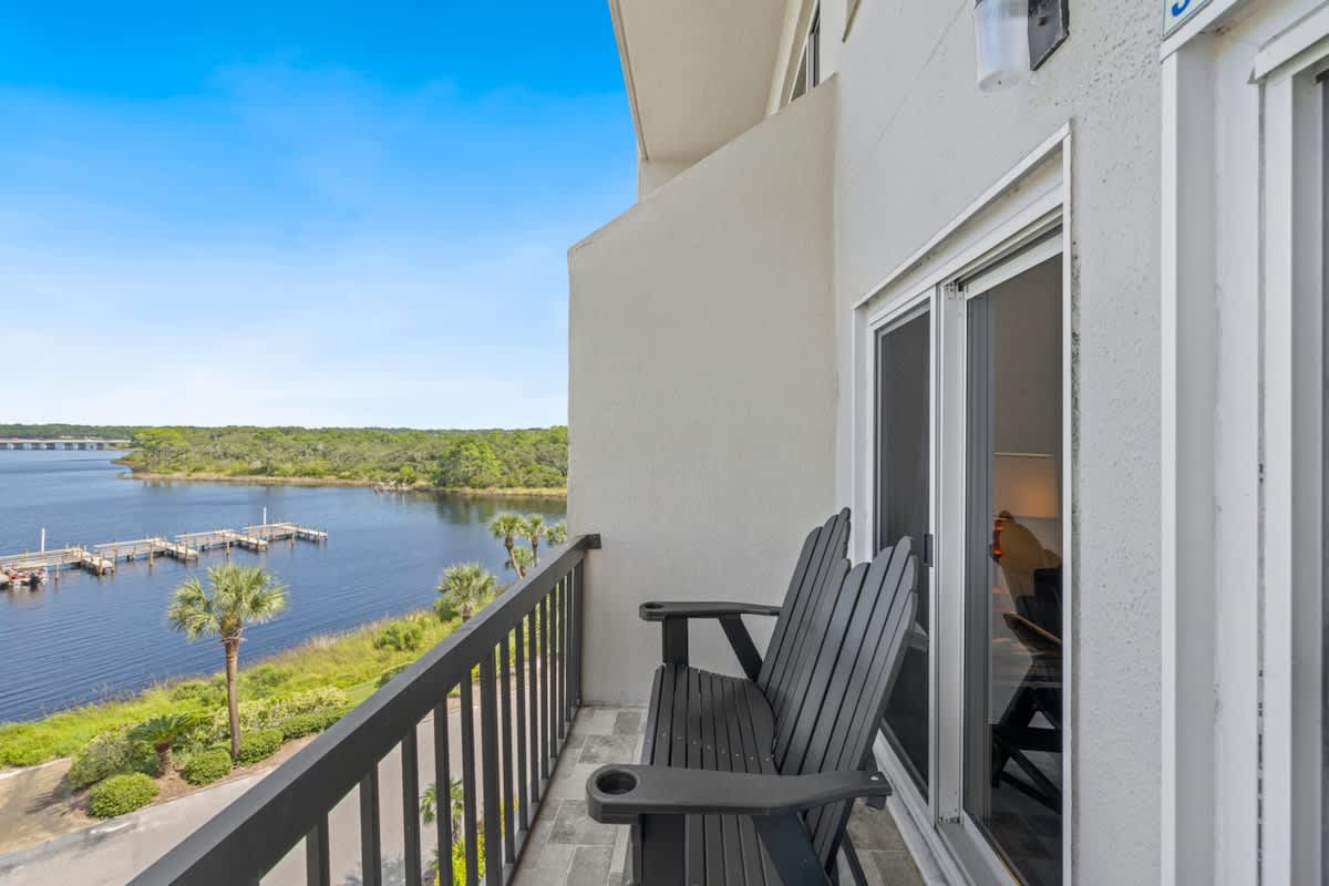 Pinnacle Port 304A – Balcony with two chairs overlooking a calm body of water and greenery.