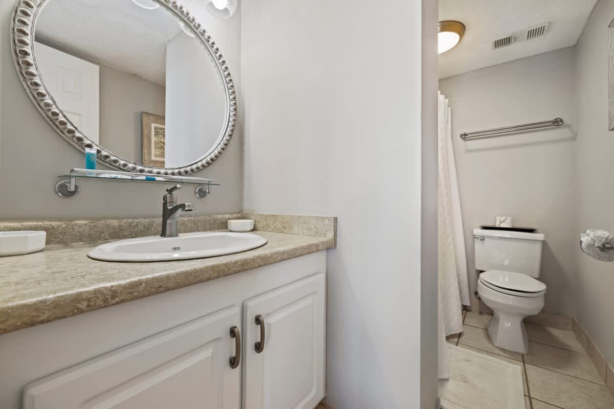 Pinnacle Port 304A – Bathroom with a round mirror, sink, toilet, and shower, featuring neutral-toned walls and tile flooring.