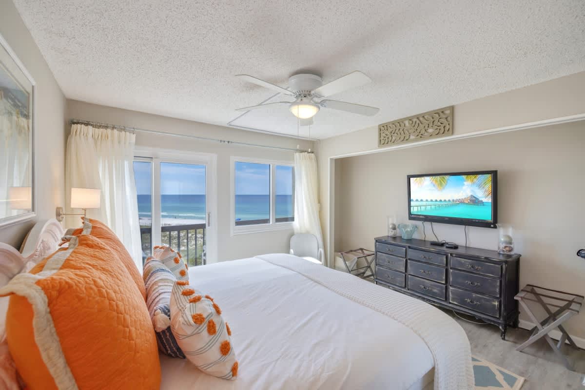 Pinnacle Port 304A – Bright bedroom with ocean view, ceiling fan, TV, and decorative pillows.