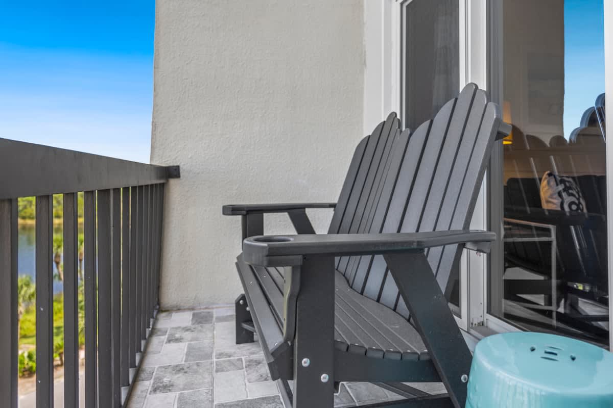 Pinnacle Port 304A – Balcony with two black Adirondack chairs and a turquoise side table overlooking water and greenery.