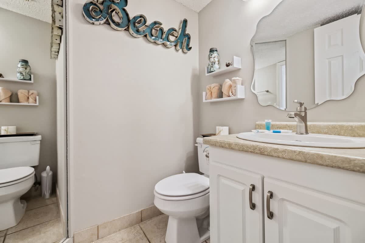 Pinnacle Port 304A – Bathroom with toilet, sink, mirror, beach-themed decor, and decorative shelving.