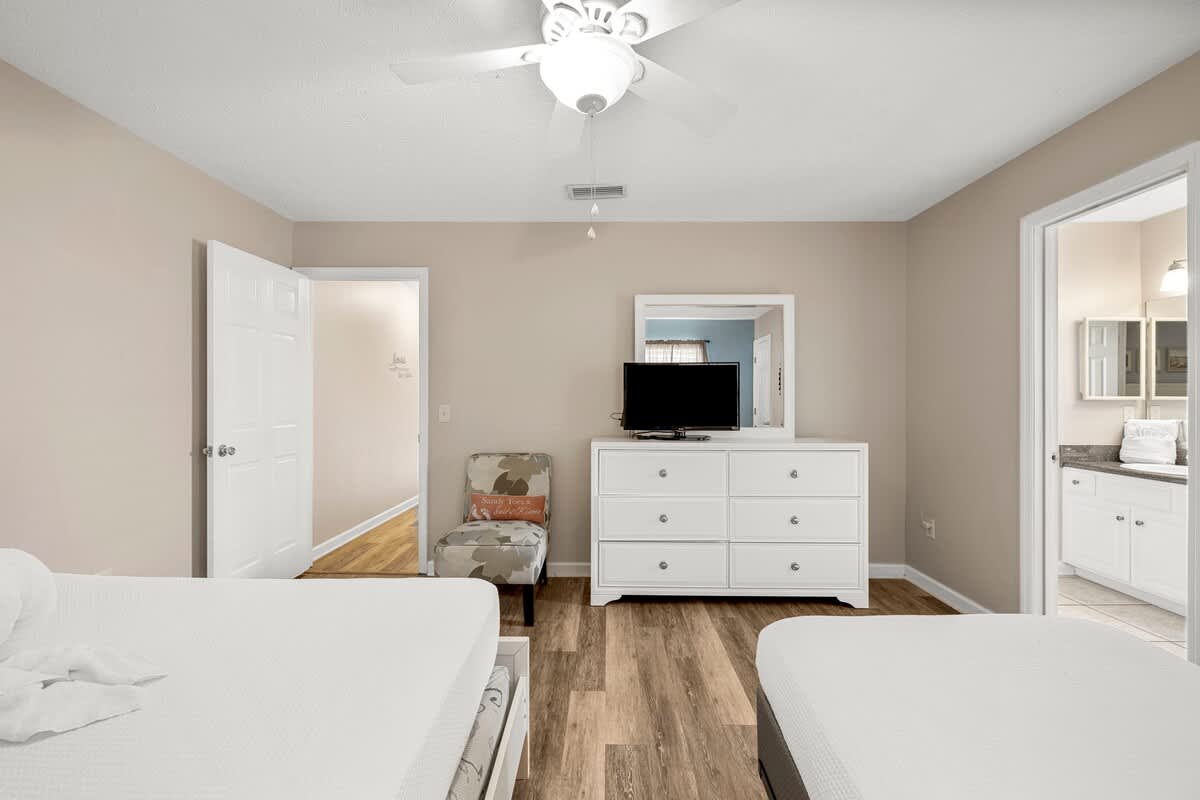 126 Seagrass Way – Bedroom with two beds, a dresser, TV, and en-suite bathroom entry. Wood flooring and a ceiling fan.