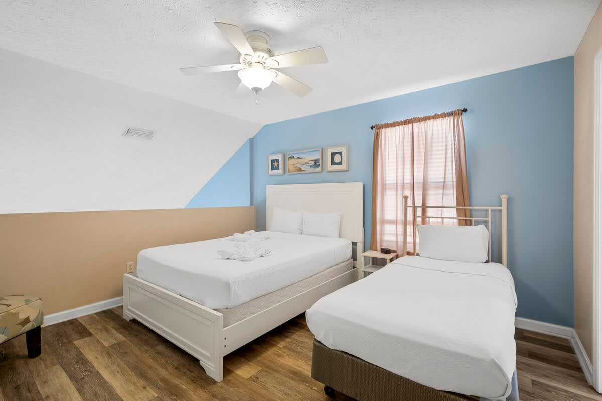 126 Seagrass Way – Bedroom with a queen bed, twin bed, blue walls, and a window with light curtains.