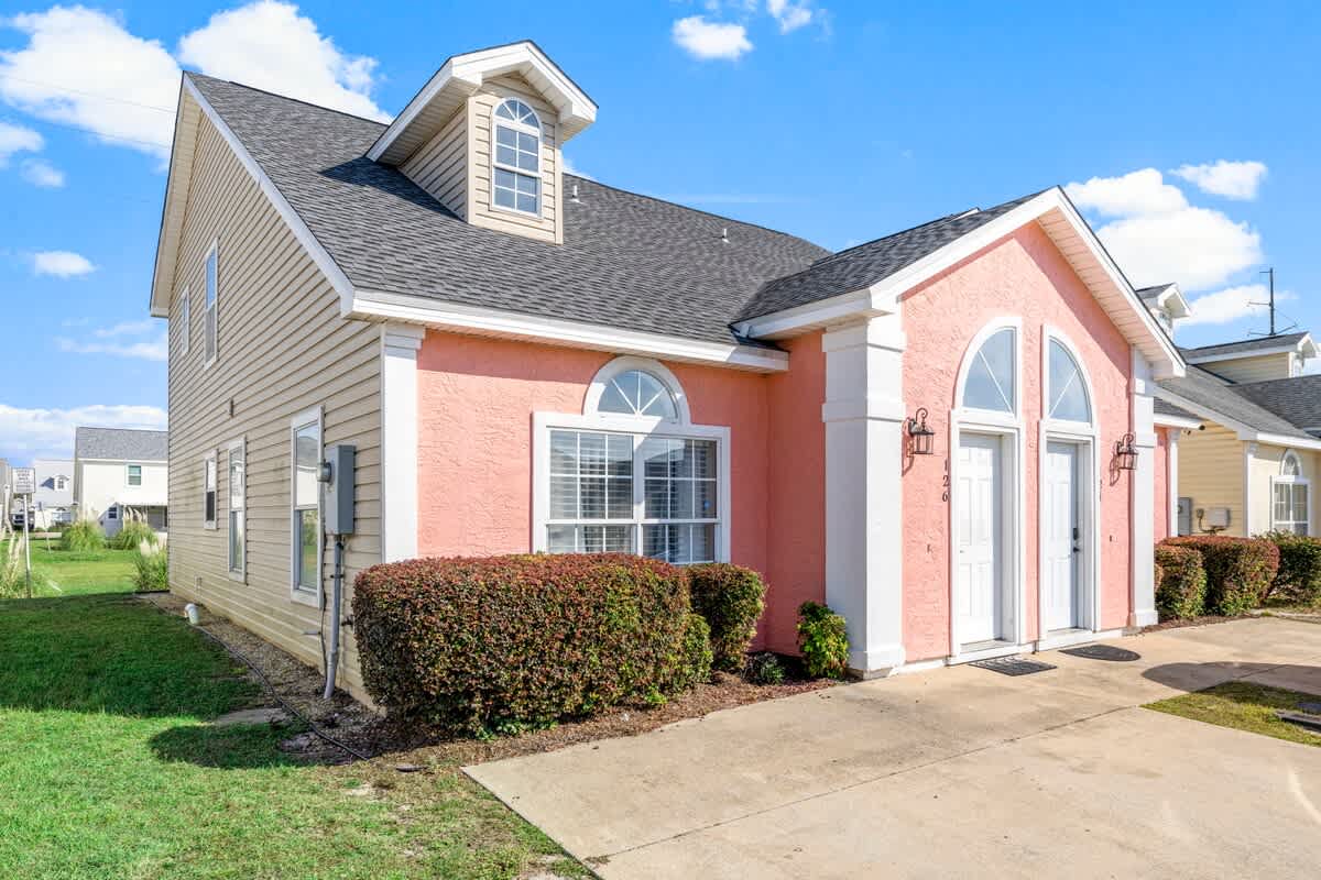 126 Seagrass Way – Single-story vacation rental with a pink exterior, two front doors, and manicured shrubs.