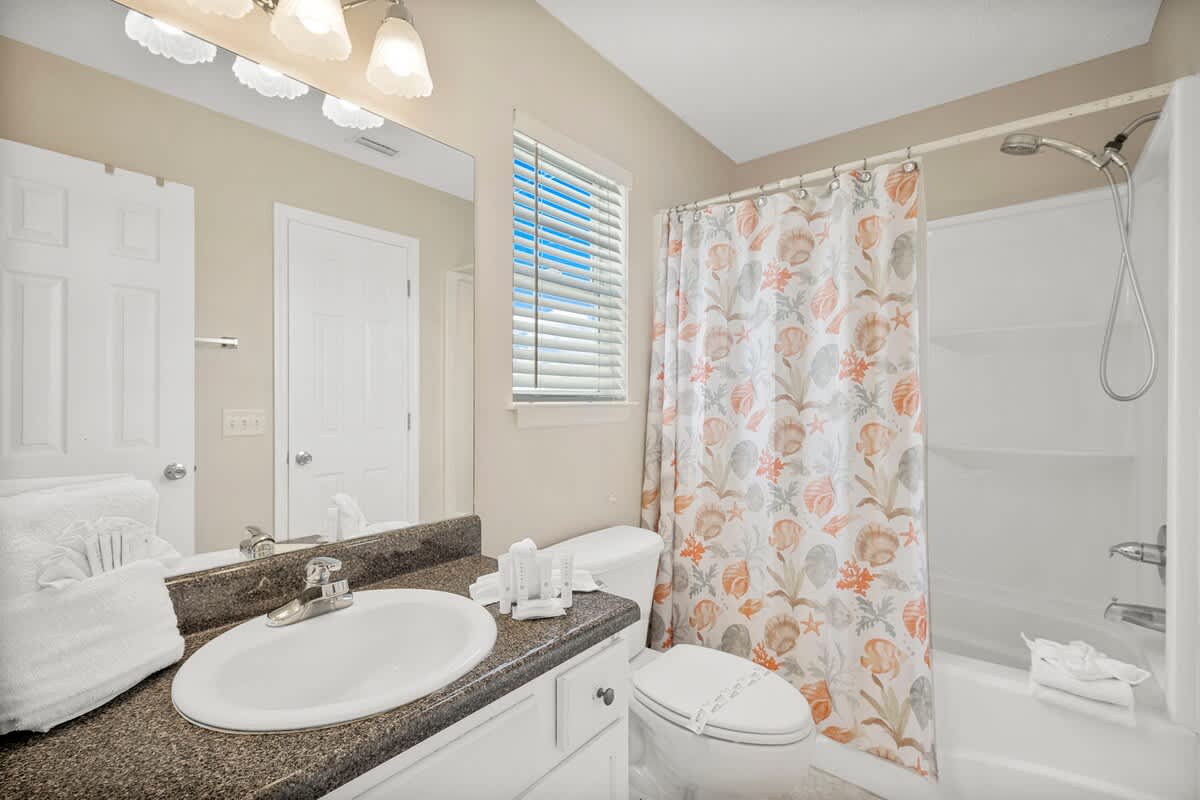 126 Seagrass Way – Bright bathroom with a sink, shower, toilet, and a patterned shower curtain.