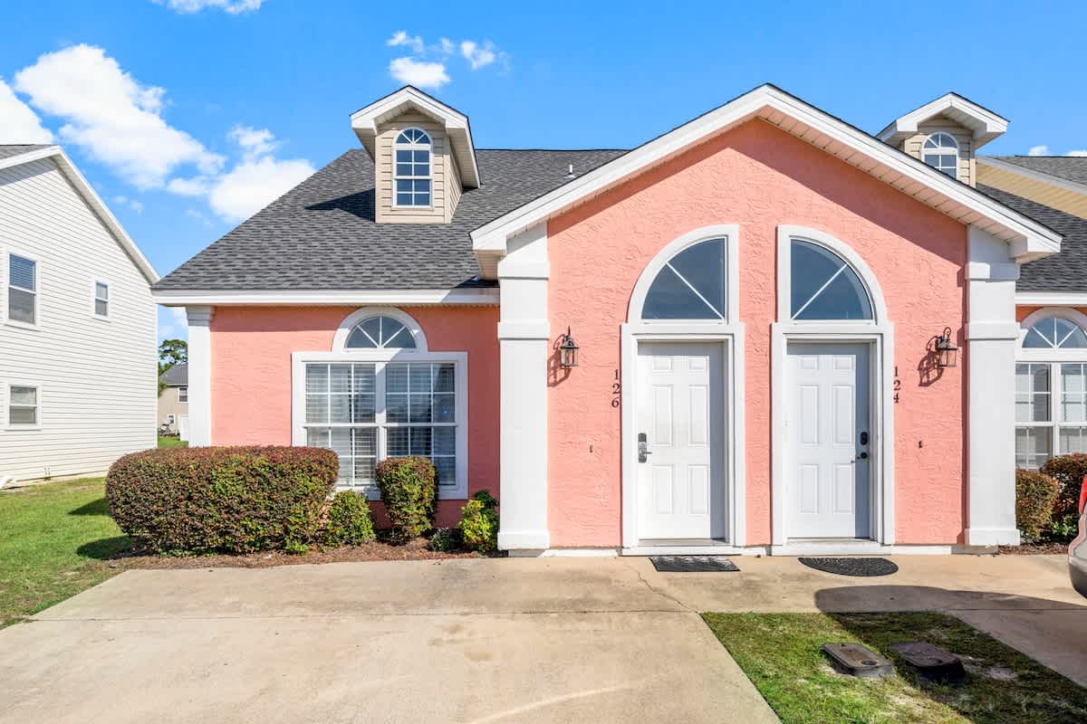 126 Seagrass Way – Exterior view of a pink duplex with two front doors and landscaped shrubs.