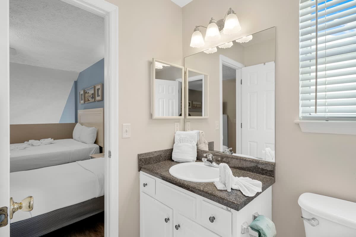 126 Seagrass Way – Bathroom with a sink, mirror, and towel; doorway into a bedroom with two beds visible.
