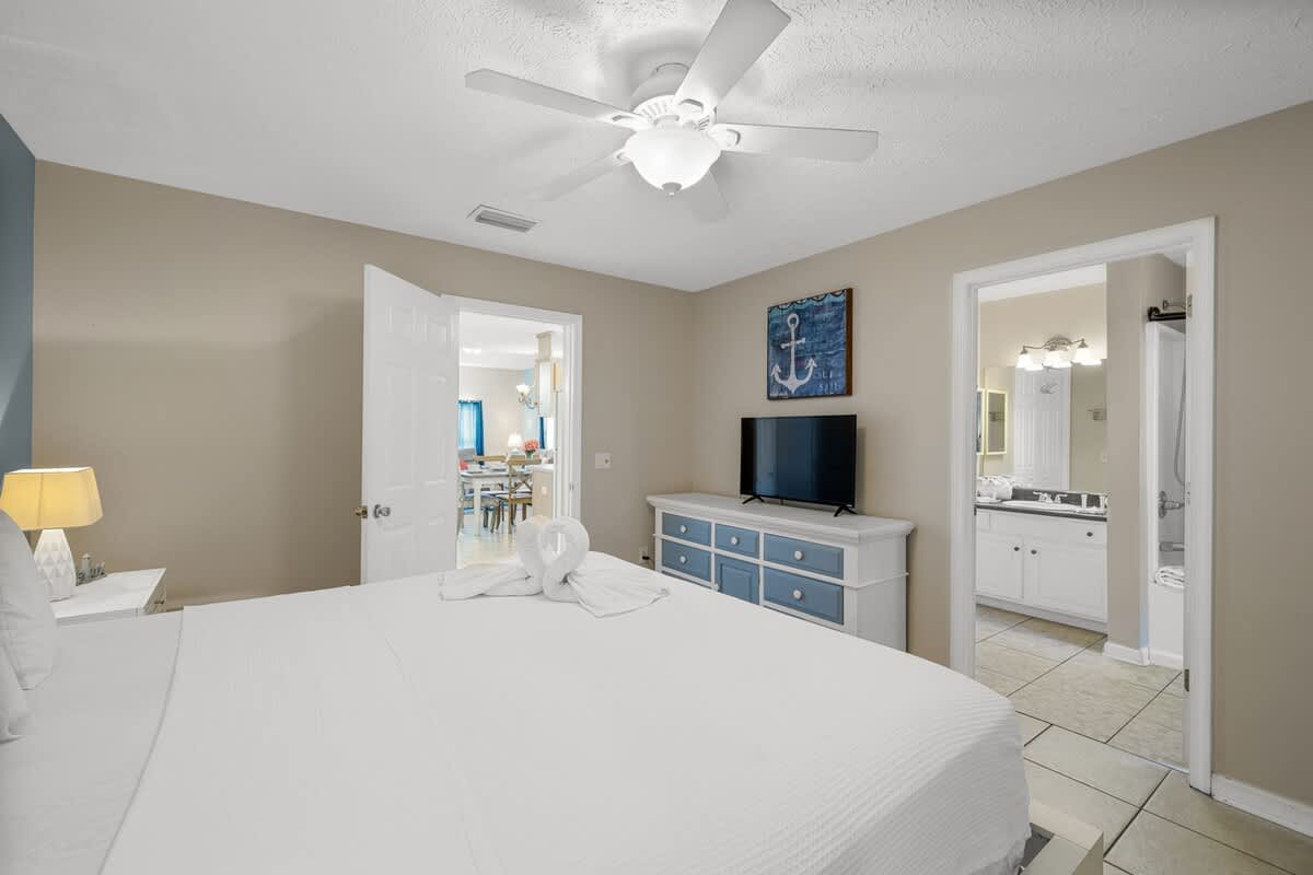 126 Seagrass Way – Bedroom with queen bed, dresser, TV, ceiling fan, doorway to bathroom, and view into living area.