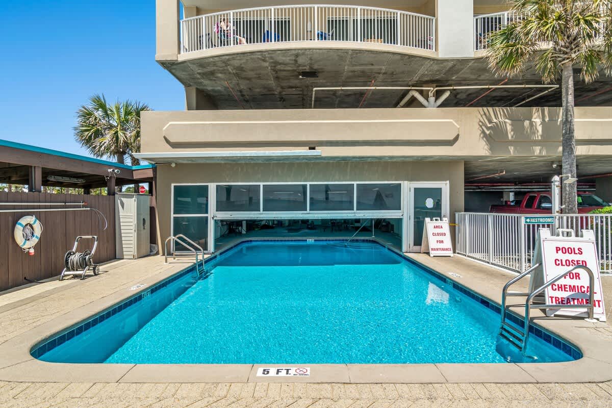 Ocean Villa 1104 – Pool area with clear water, adjacent building, and safety signage in bright sunlight.