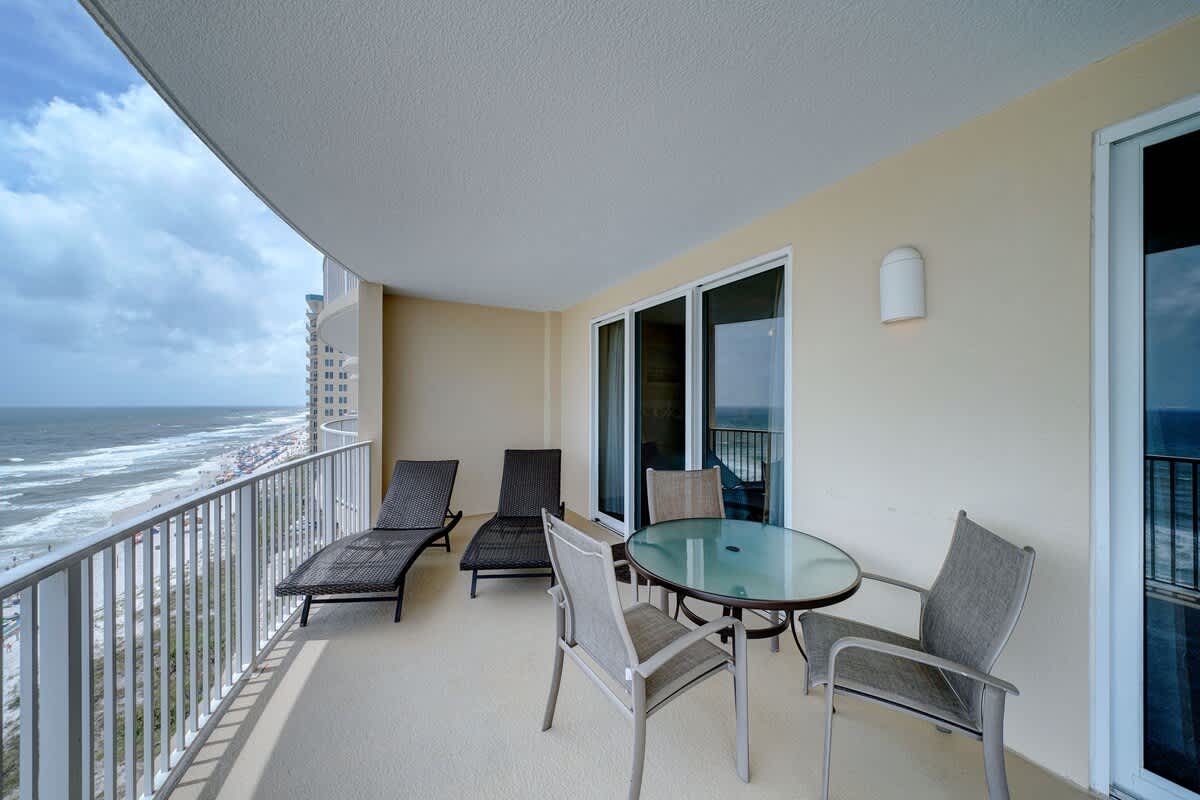 Ocean Villa 1104 – Balcony with ocean view, two lounge chairs, and a glass table with four chairs.