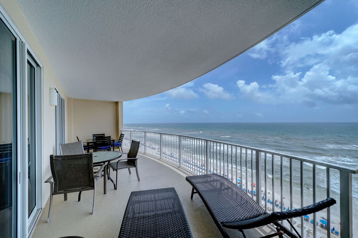 Ocean Villa 1104 – Balcony with outdoor seating and ocean view over sandy beach with umbrellas.