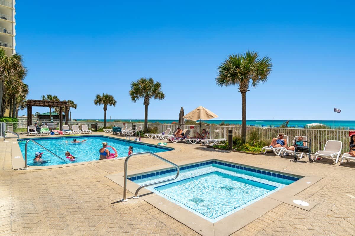 Ocean Villa 1104 – Pool area with two swimming pools, lounge chairs, palm trees, and ocean view in the background.