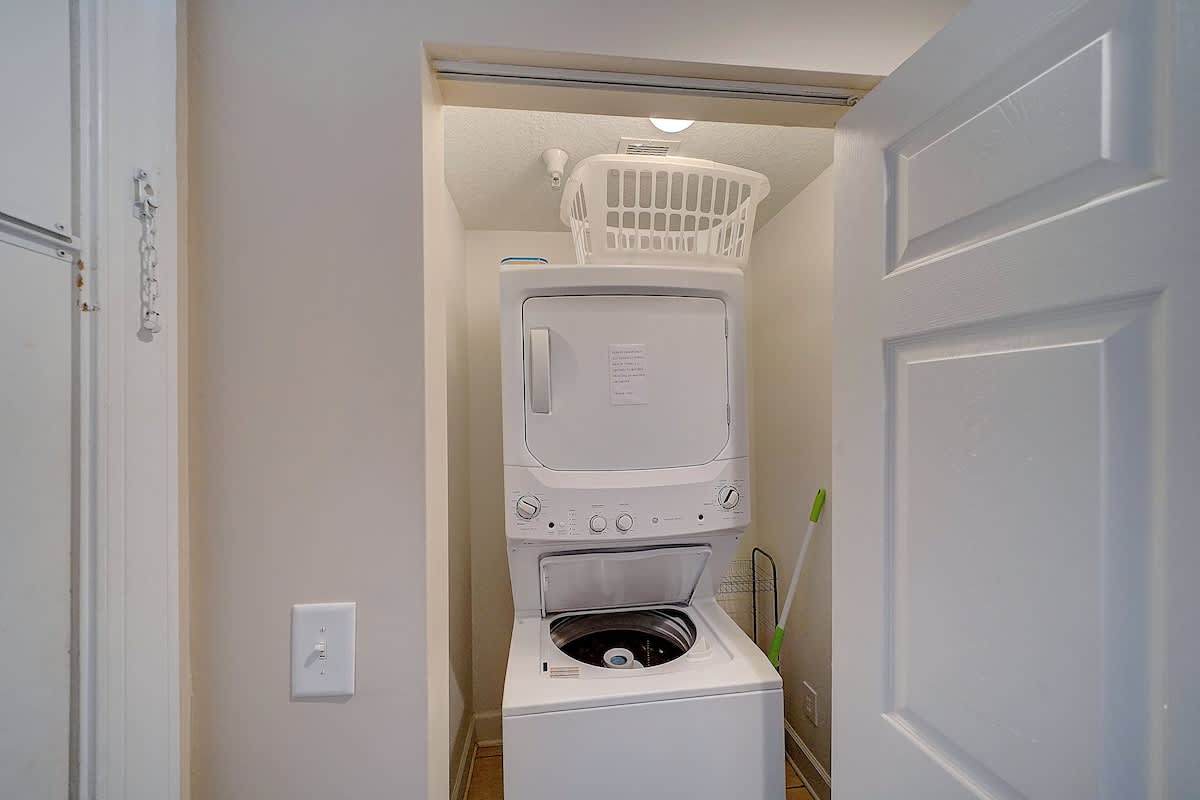 Ocean Villa 1104 – Laundry closet featuring a stacked washer and dryer with a laundry basket on top.