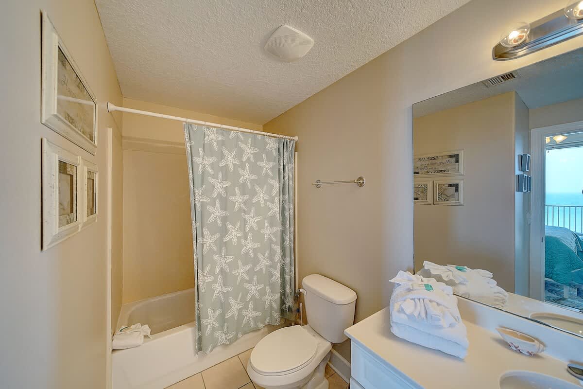 Ocean Villa 1104 – Bathroom featuring a shower-tub combo, toilet, sink, and starfish-patterned shower curtain.