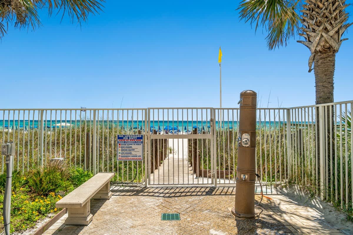 Ocean Villa 1104 – Gated entrance to beach with view of ocean, palm trees, and pathway.