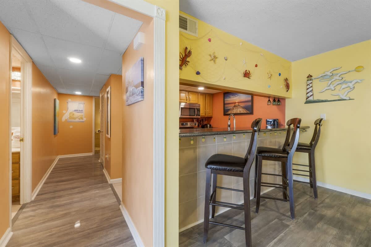 Moondrifter 207 – Interior view of a vacation rental with an open kitchen and bar seating, featuring warm colors and coastal decor.
