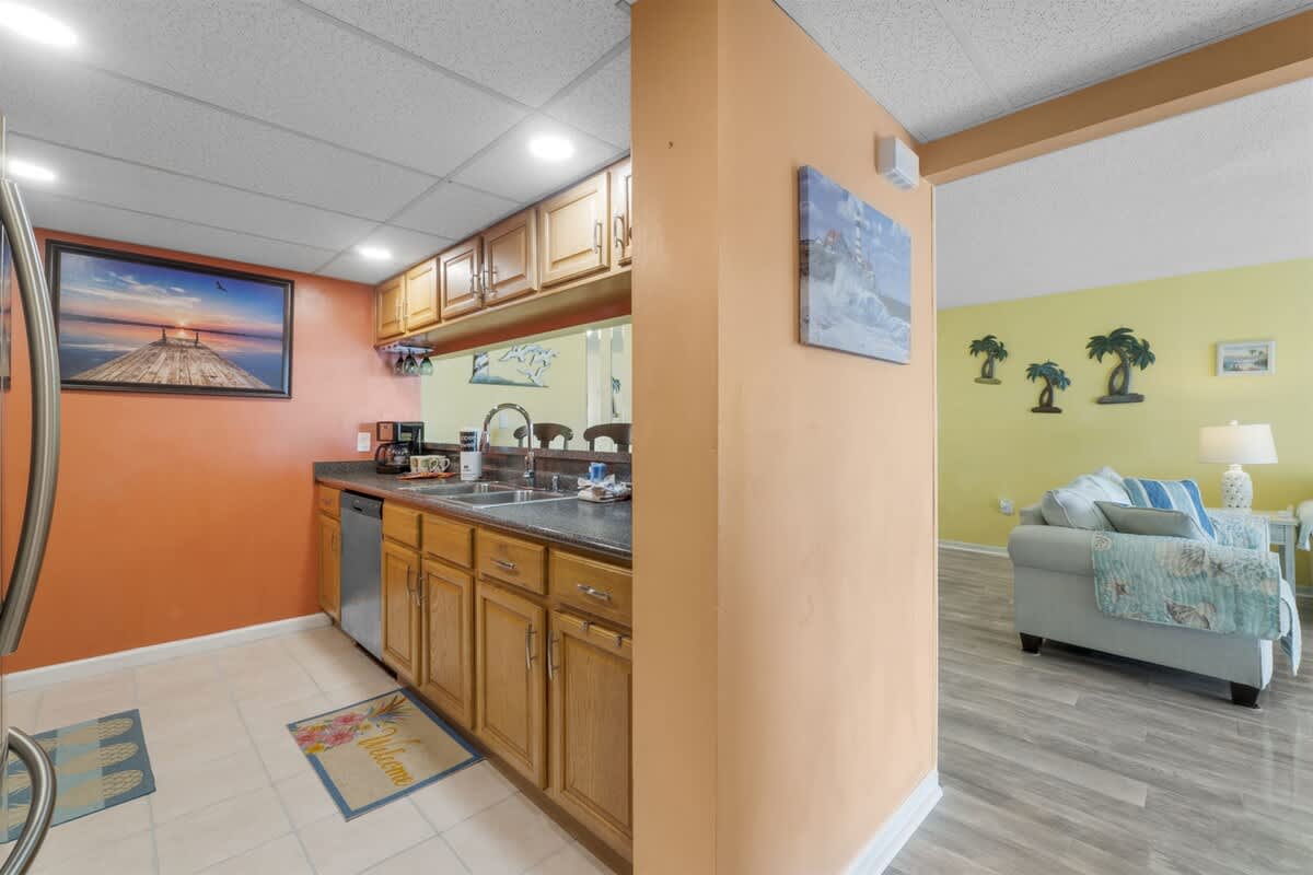 Moondrifter 207 – Cozy kitchen area with wooden cabinets and a living space featuring light-colored furniture and tropical decor.