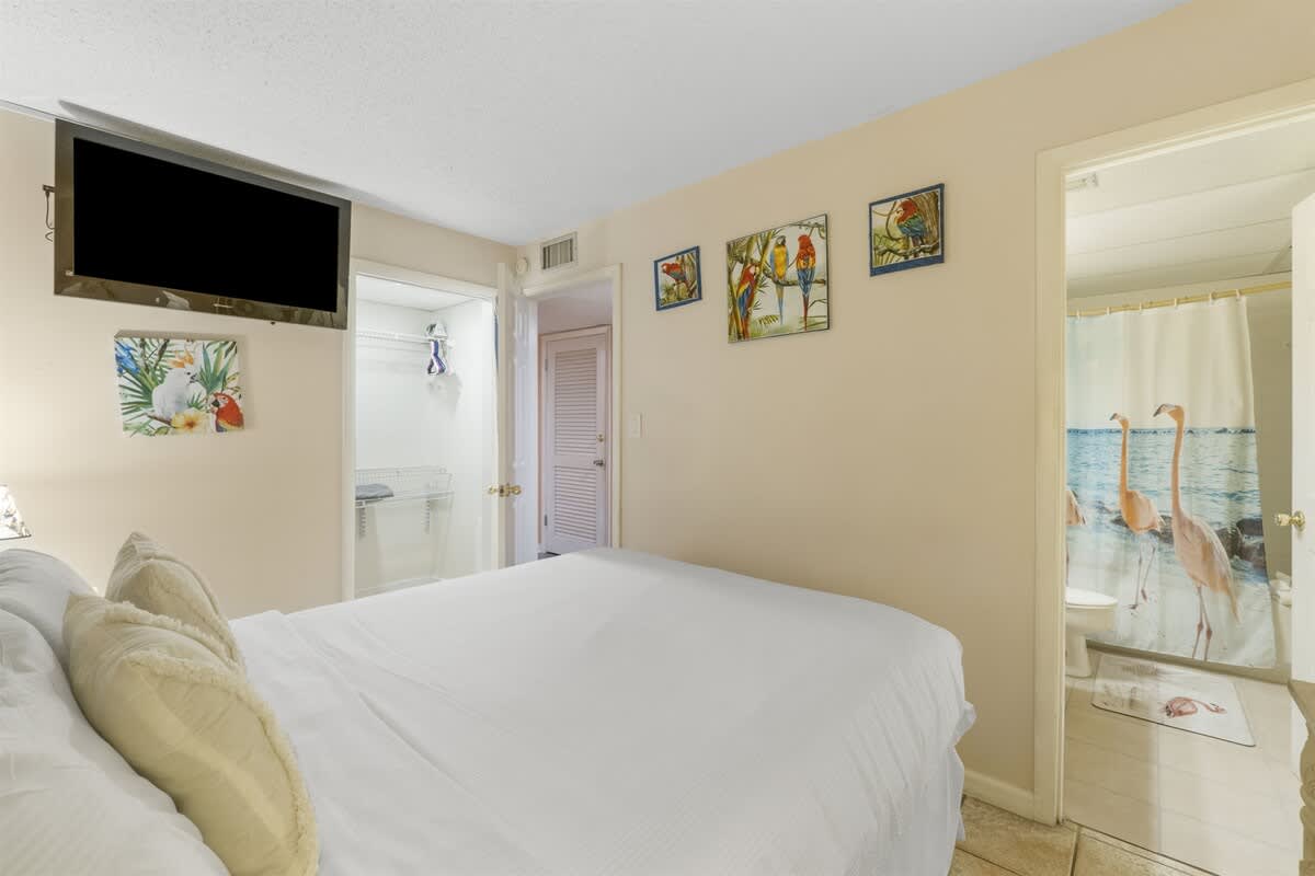 Moondrifter 207 – Bedroom with white bedding, TV mounted on wall, closet, and bathroom visible through open door with floral shower curtain.