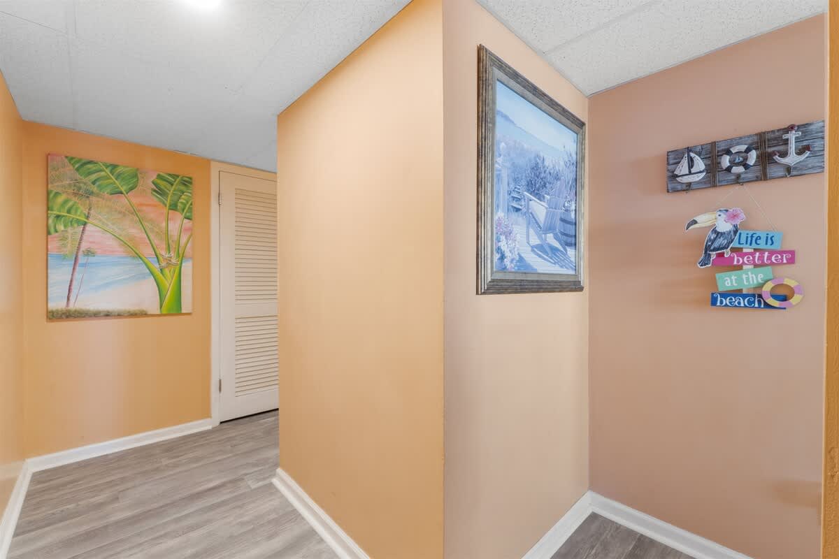 Moondrifter 207 – Hallway with peach walls, framed beach-themed artwork, wooden sign, and closet door.