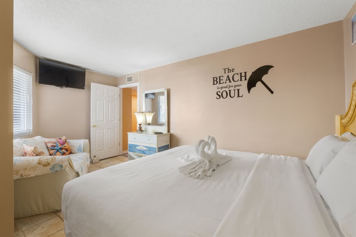 Moondrifter 207 – Bright bedroom with a king bed, decorative towels, a TV, and a couch near the window.