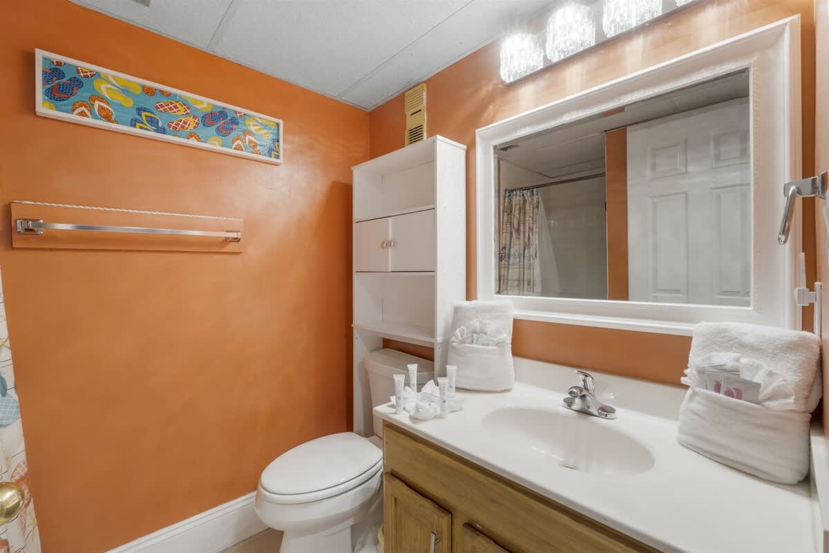 Moondrifter 207 – Bright orange bathroom with a sink, mirror, towels, and a shower behind a curtain.