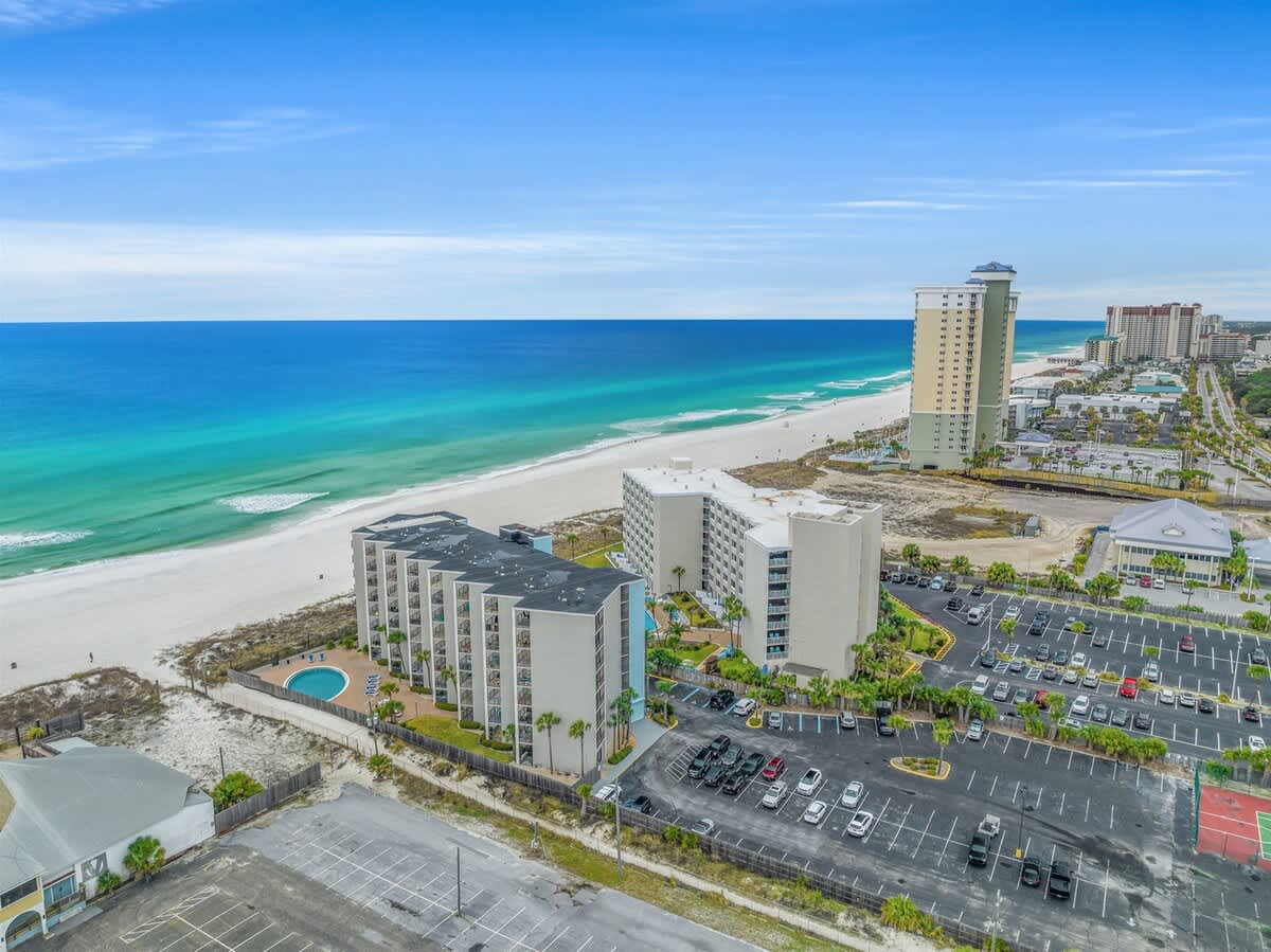 Moondrifter 207 – Aerial view of beachside rental with pool, parking lot, and ocean in the background.