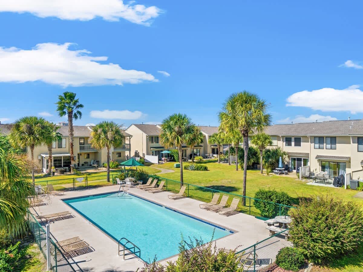 135 Grande Island Blvd – View of a swimming pool surrounded by lounge chairs and palm trees, with vacation rental units in the background.