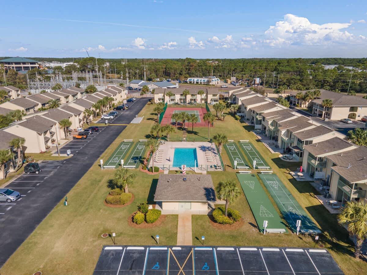 135 Grande Island Blvd – Aerial view of vacation rental complex with pool, tennis courts, and row of buildings surrounded by greenery.