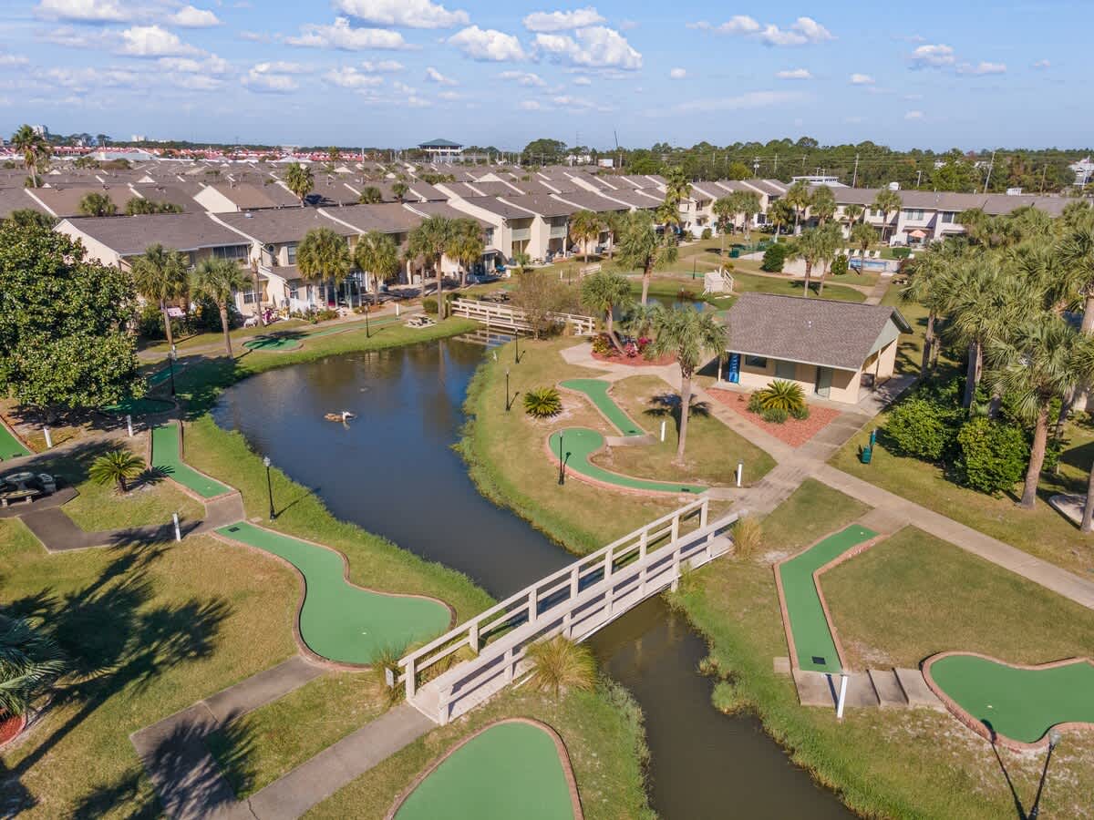 135 Grande Island Blvd – Drone view of vacation rental community with green mini-golf, pond, and pathways surrounded by palm trees.