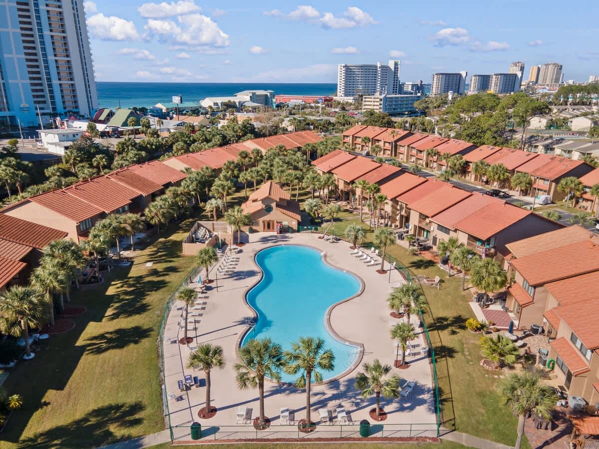 135 Grande Island Blvd – Aerial view of a pool surrounded by vacation rental units and palm trees, with ocean in the background.