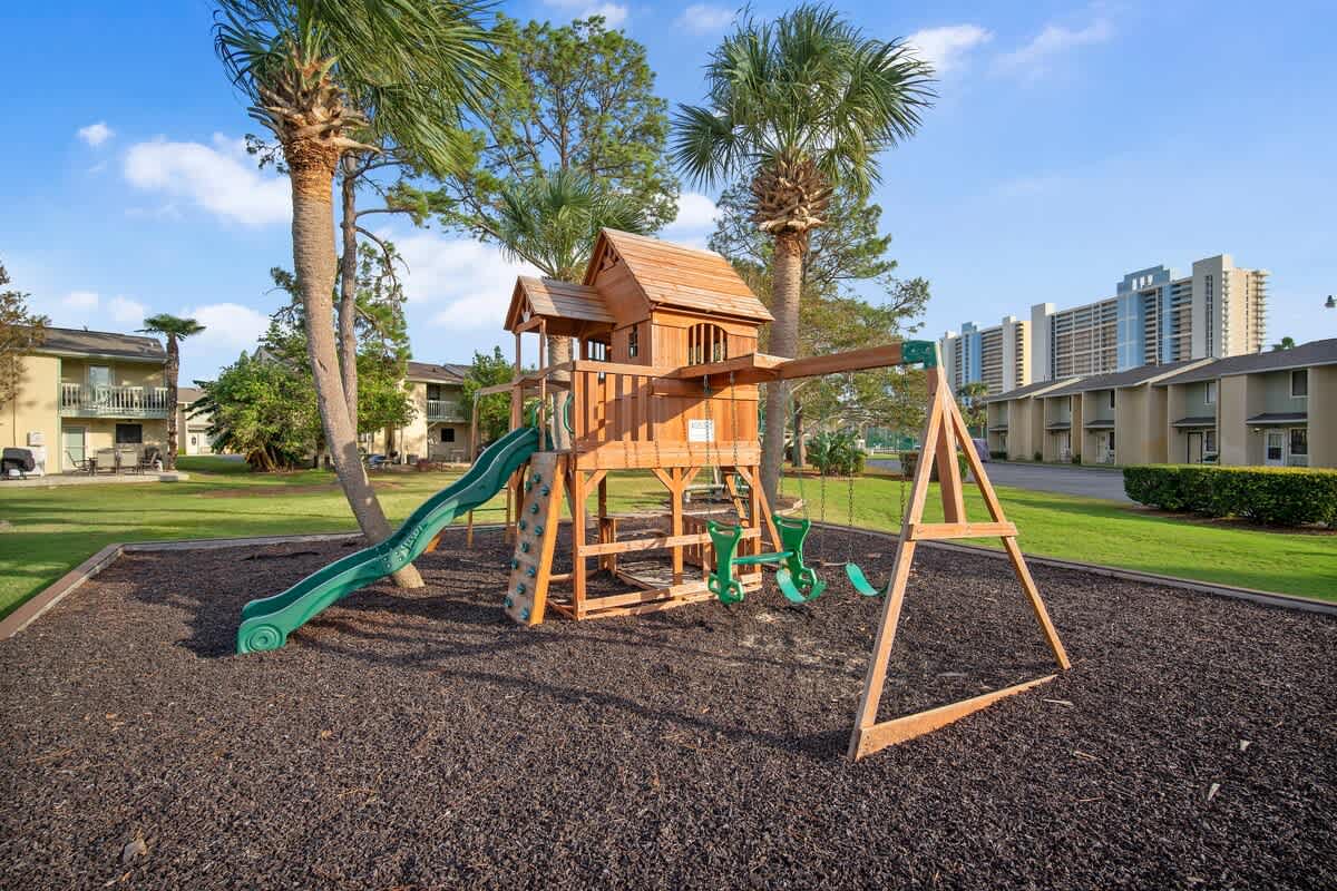 135 Grande Island Blvd – Wooden playground structure with slide and swings, surrounded by green grass and palm trees.