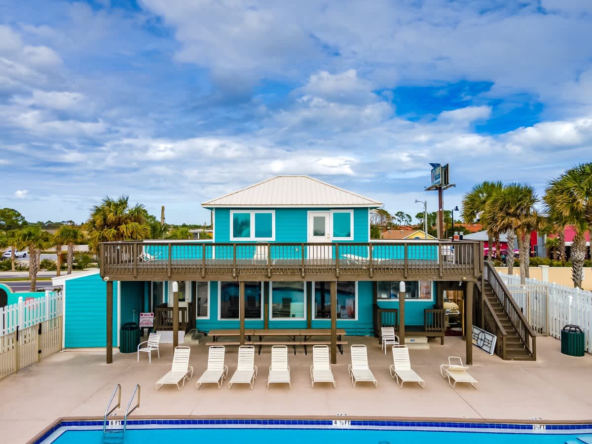 135 Grande Island Blvd – Two-story blue vacation rental with outdoor seating, poolside loungers, and a deck overlooking the pool.
