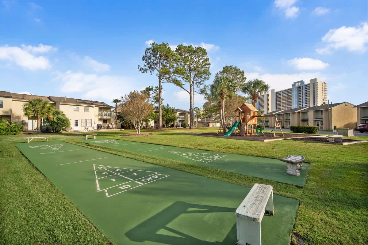 135 Grande Island Blvd – Green lawn with shuffleboard courts, playground, and nearby apartment buildings under a blue sky.