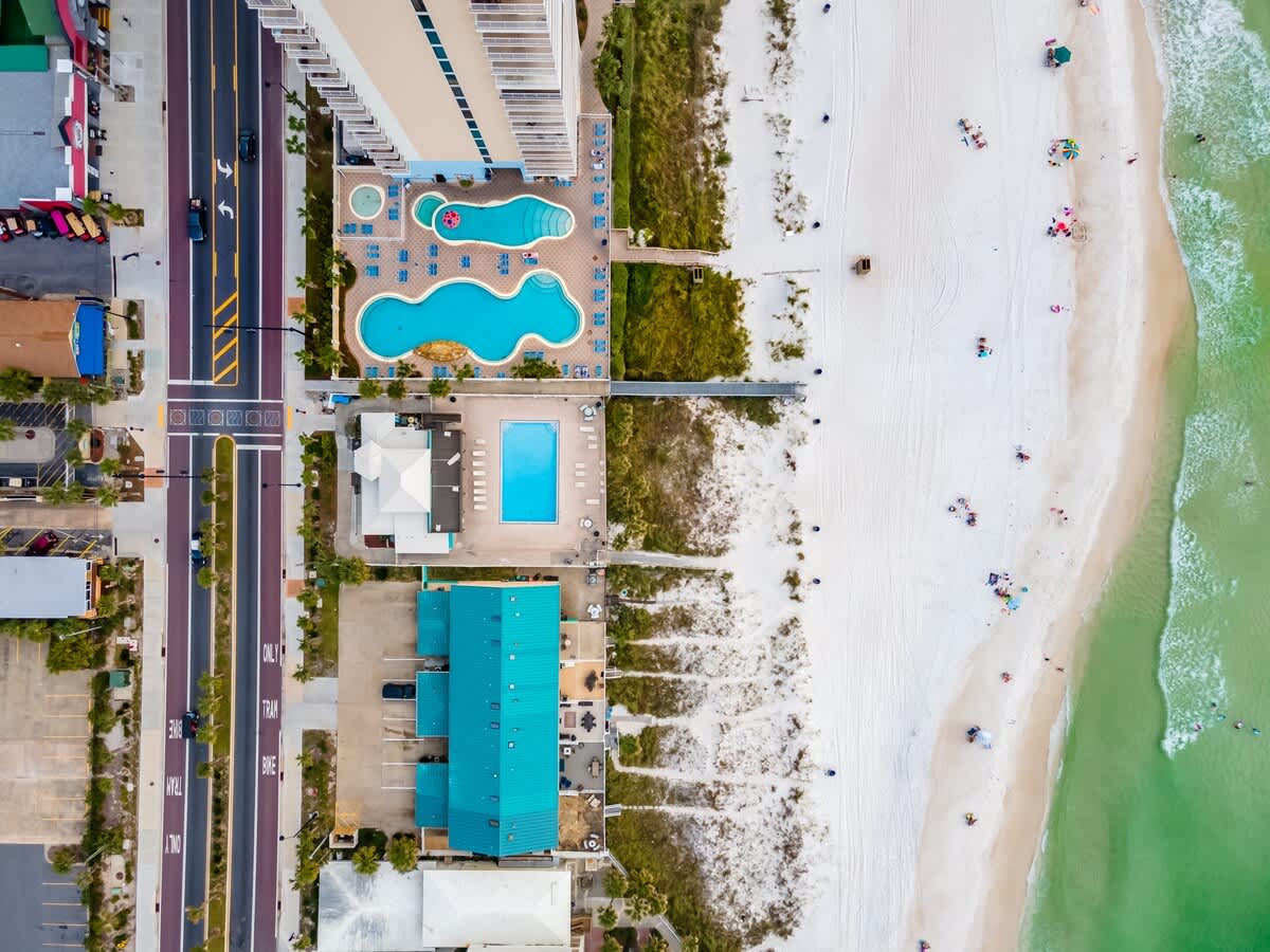 135 Grande Island Blvd – Aerial view of a beach, pool area, and nearby buildings with tropical landscaping.