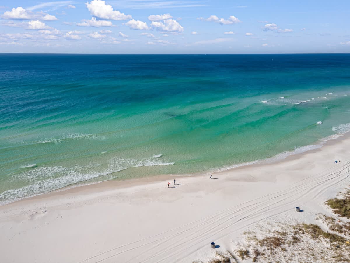 135 Grande Island Blvd – Aerial view of a beach with white sand, turquoise water, and people walking along the shore.