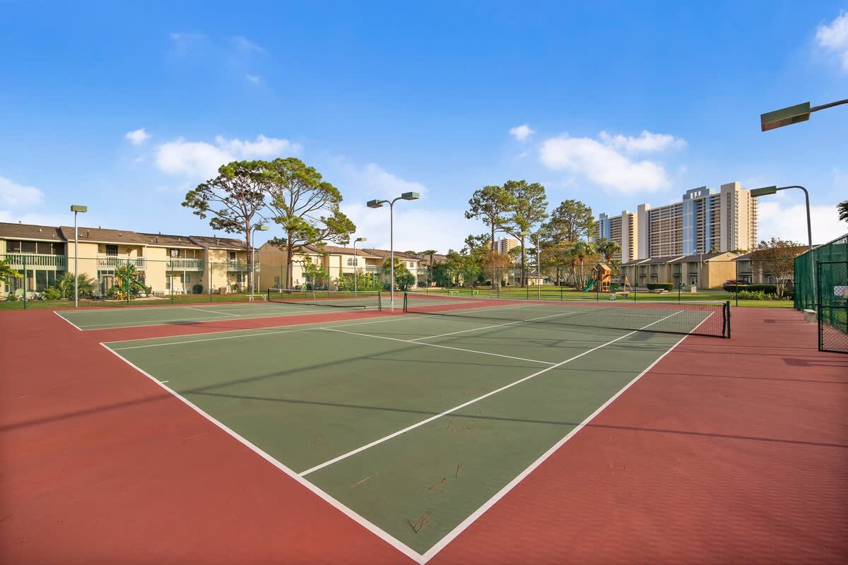 135 Grande Island Blvd – Tennis courts with green and red surfaces, surrounded by residential buildings and tall trees.