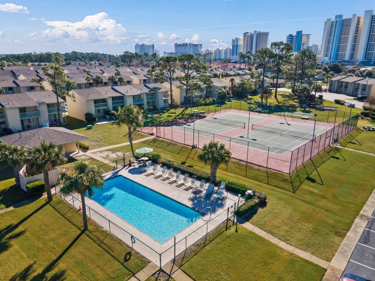 135 Grande Island Blvd – Aerial view of a pool, tennis courts, and surrounding apartment buildings on a sunny day.