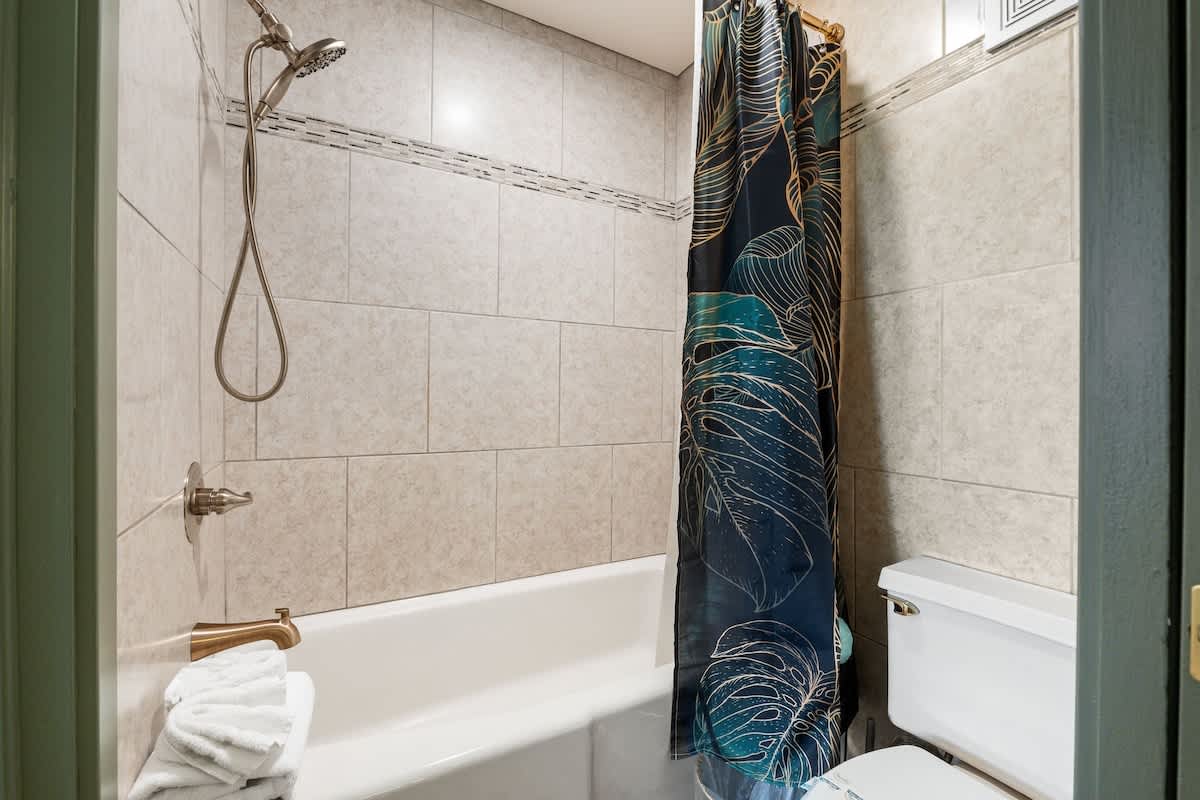 The Summit 1107 – Bathroom featuring a bathtub, showerhead, decorative curtain, and toilet.