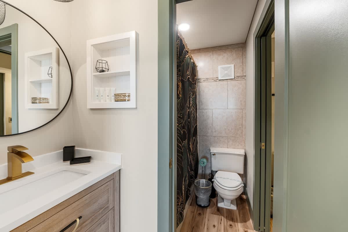 The Summit 1107 – Modern bathroom featuring a sink, storage shelf, shower curtain, and toilet. Wood-like flooring visible.