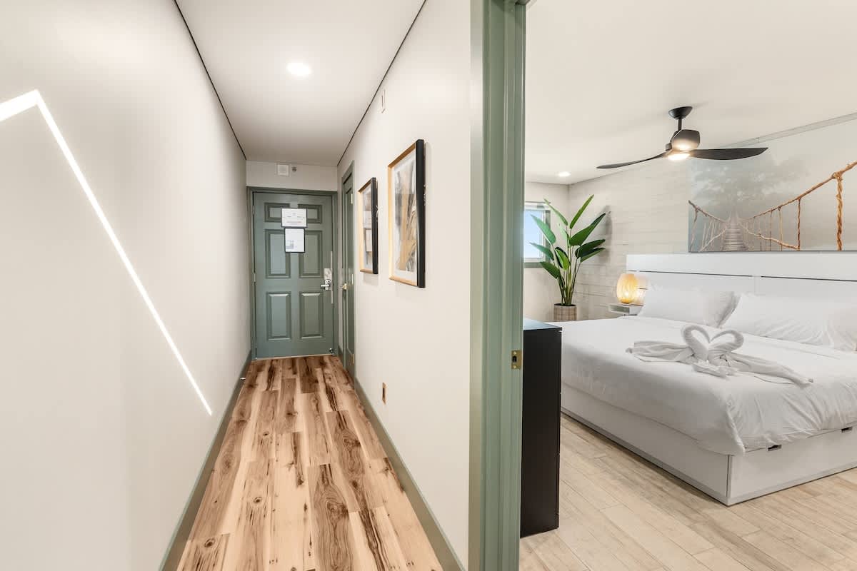 The Summit 1107 – Hallway leading to a bedroom with a bed, plant, and modern décor.