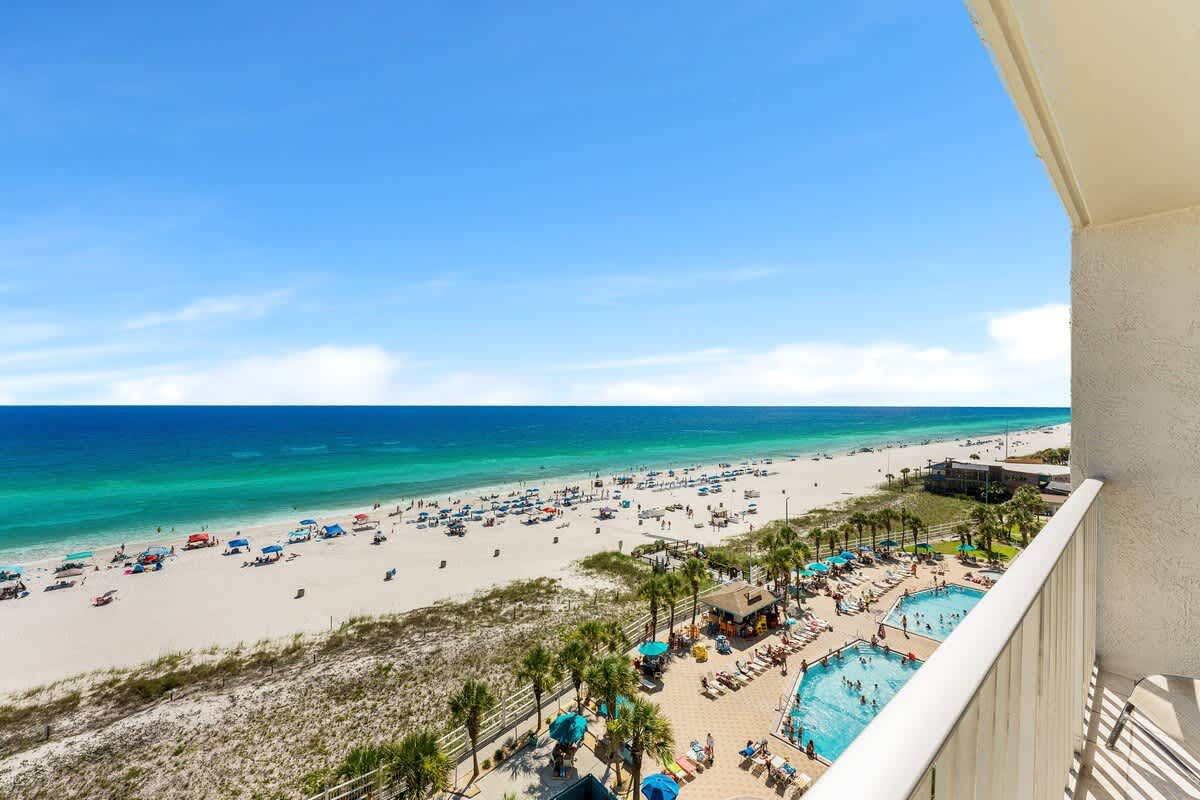 The Summit 927 – Ocean view from the balcony overlooking a sandy beach with umbrellas and pools below.