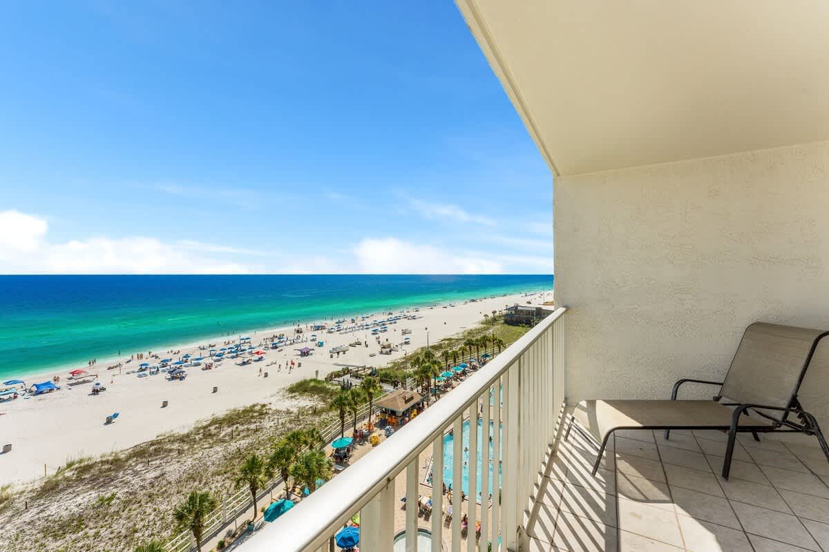 The Summit 927 – Balcony view of beach, ocean, and pool area with chairs and umbrellas.