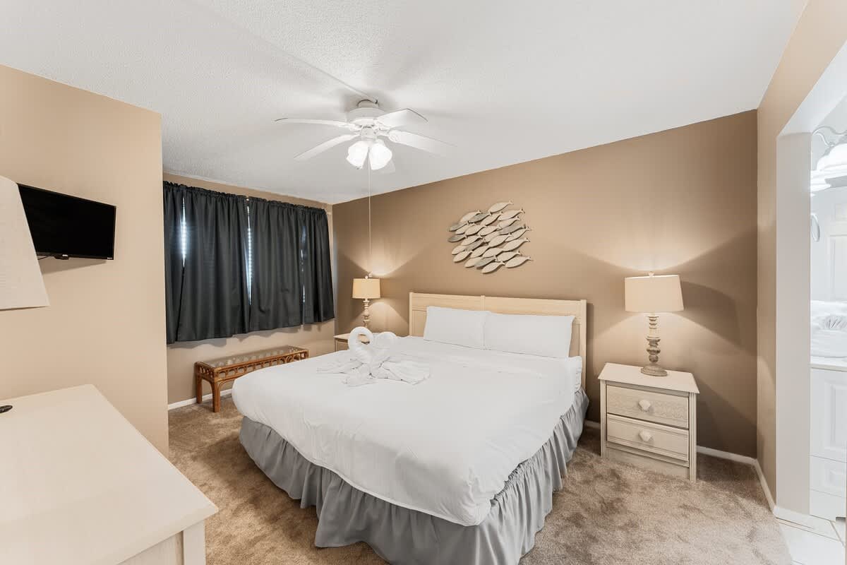 The Summit 927 – Cozy bedroom with a king bed, nightstands, lamp, dark curtains, and a TV mounted on the wall.