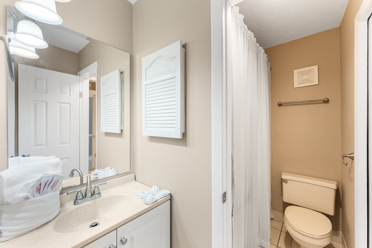 The Summit 927 – Bathroom with sink, mirror, and shower separated by a curtain. Beige walls and tiled floor.